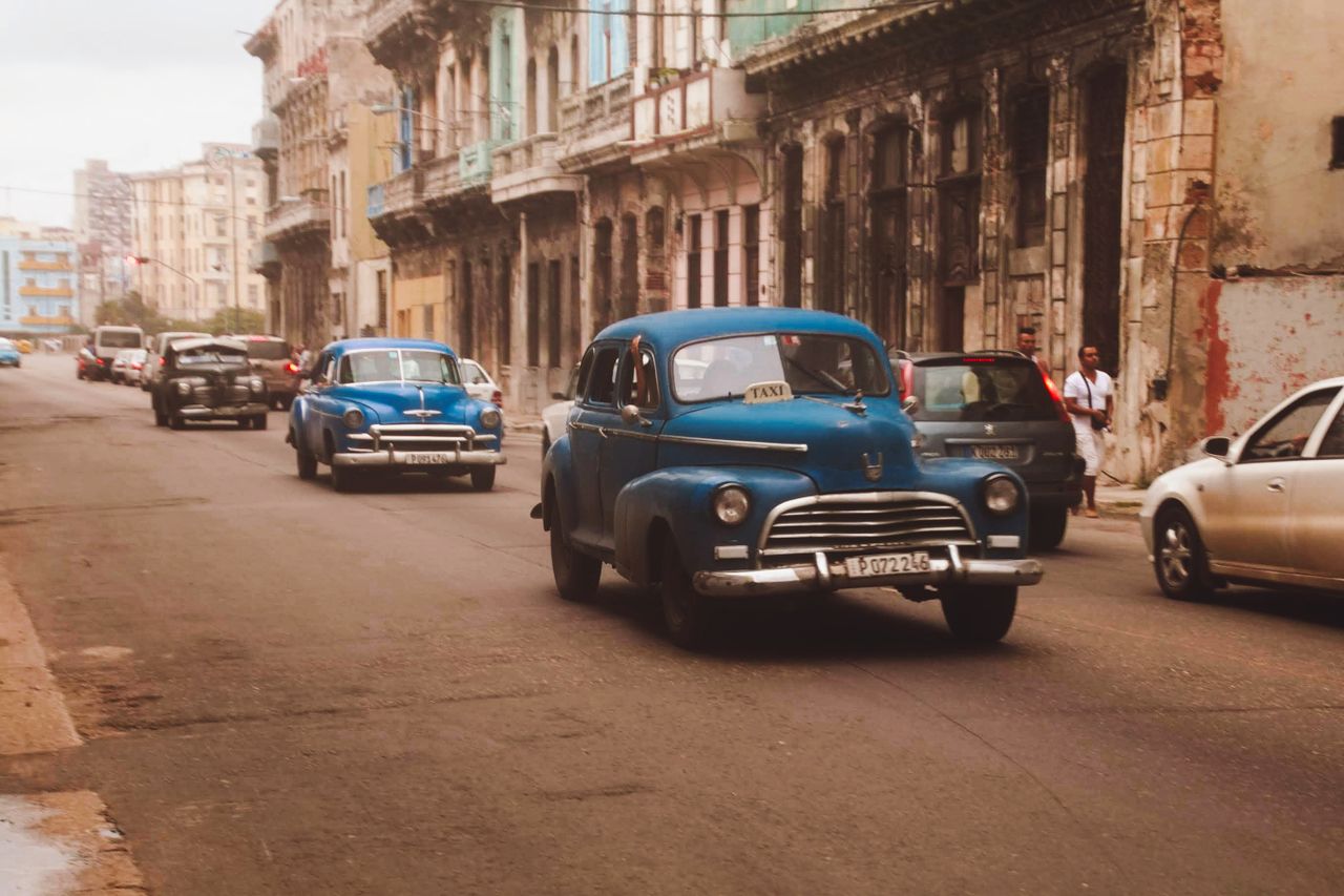 Vintage blue cars driving on a street in Cuba, showcasing classic automotive style.