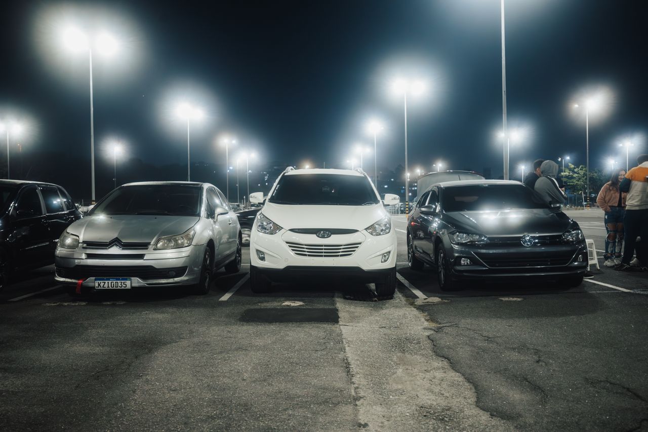 Services Night scene in a well-lit parking lot featuring various parked cars and street lamps.