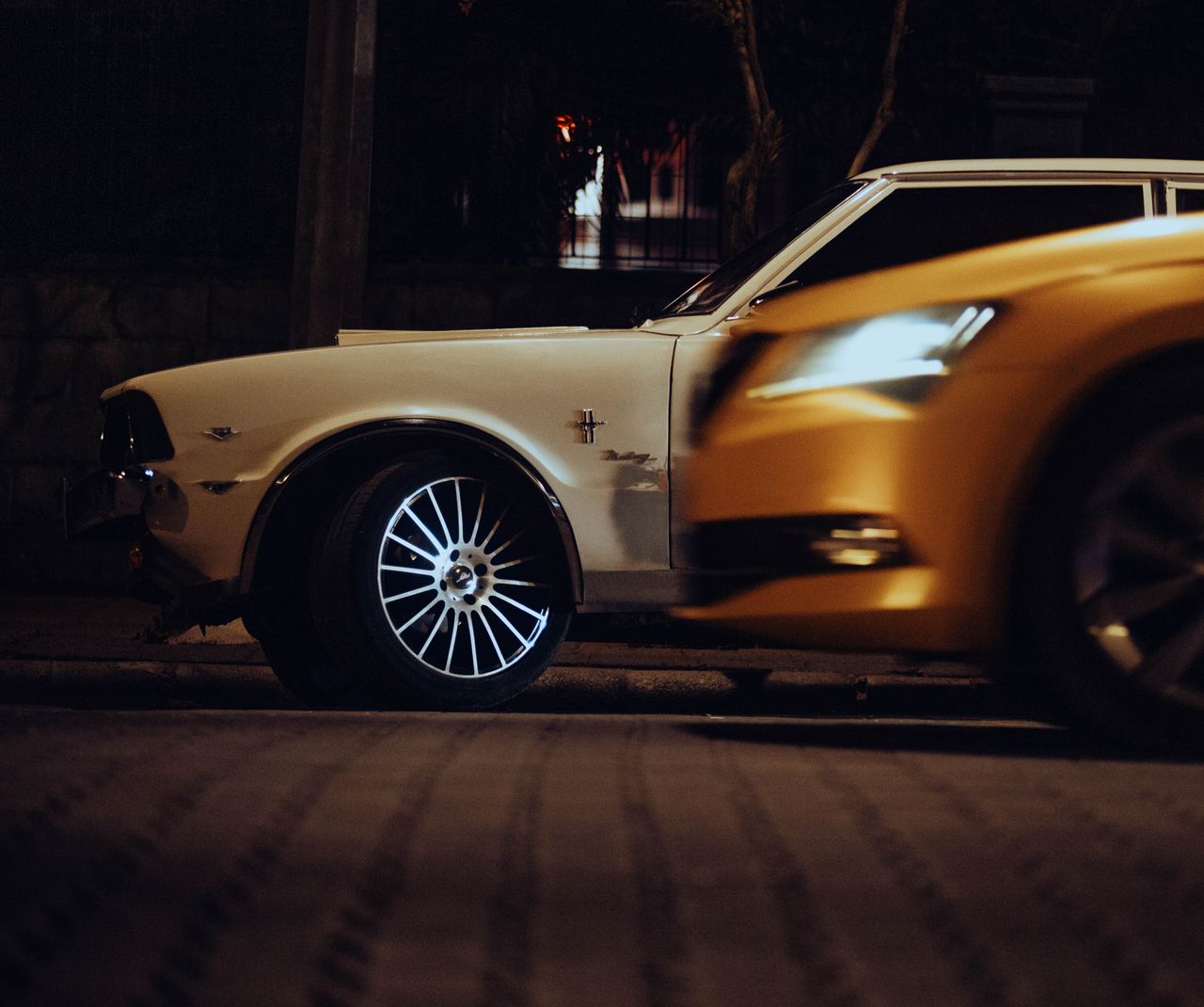 Close-up of contrasting vintage and modern cars parked on a city street at night.