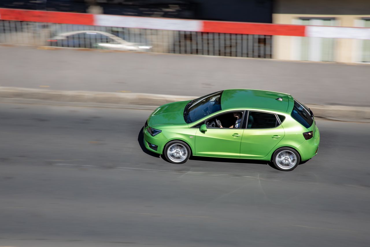 A vibrant green car speeds on an urban road, creating a motion effect.